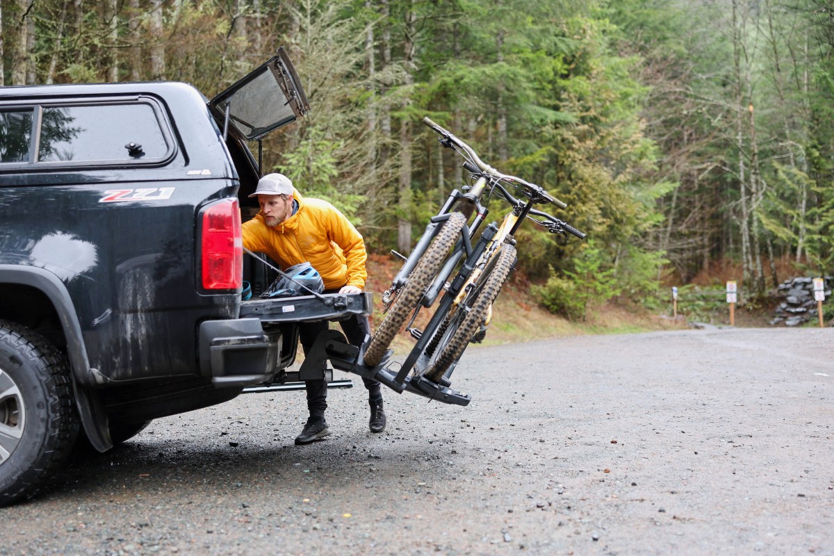 Yakima StageTwo bike rack tilted down and rider grabbing gear out of back of pickup truck.