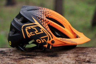 Black and orange Troy Lee Designs A2 mountain bike helmet sitting on a log.