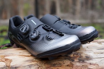 Black Shimano XC7 mountain bike shoes 3/4 profile sitting on a log.