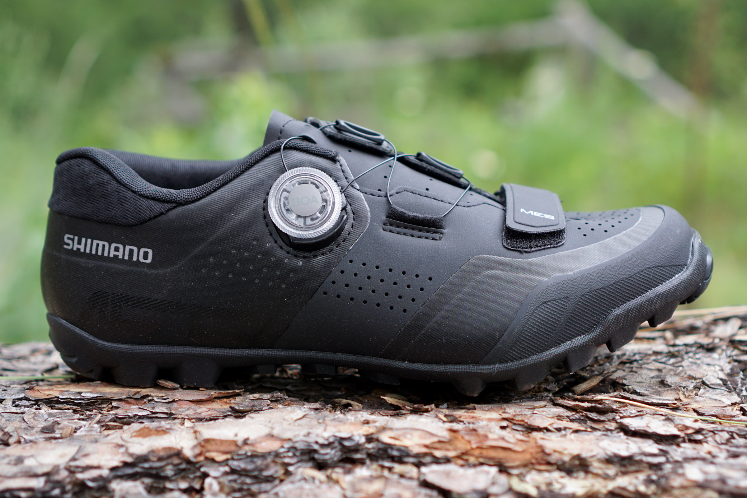 Side view of black Shimano ME5 mountain bike shoes sitting on a log.