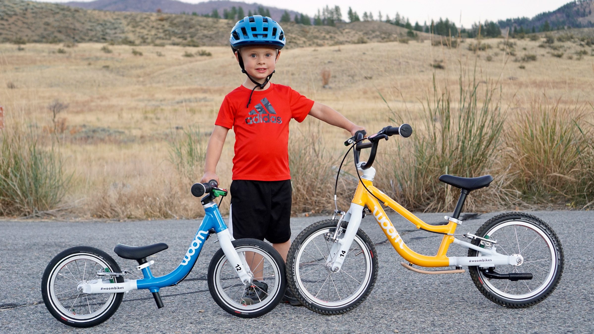 Toddler holding the Woom 1 and Woom 1 Plus balance bikes next to each other.